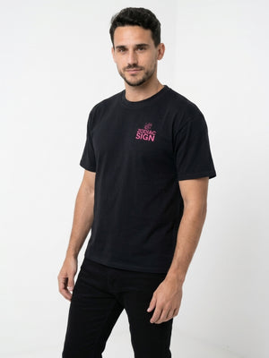 Model wearing a black premium t-shirt featuring a small pink Zodiac Sign slogan print on the chest