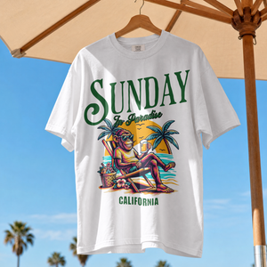 Model wearing a white relaxed fit t-shirt with a vintage green Sunday in Paradise slogan and a colorful beach sunset monkey graphic