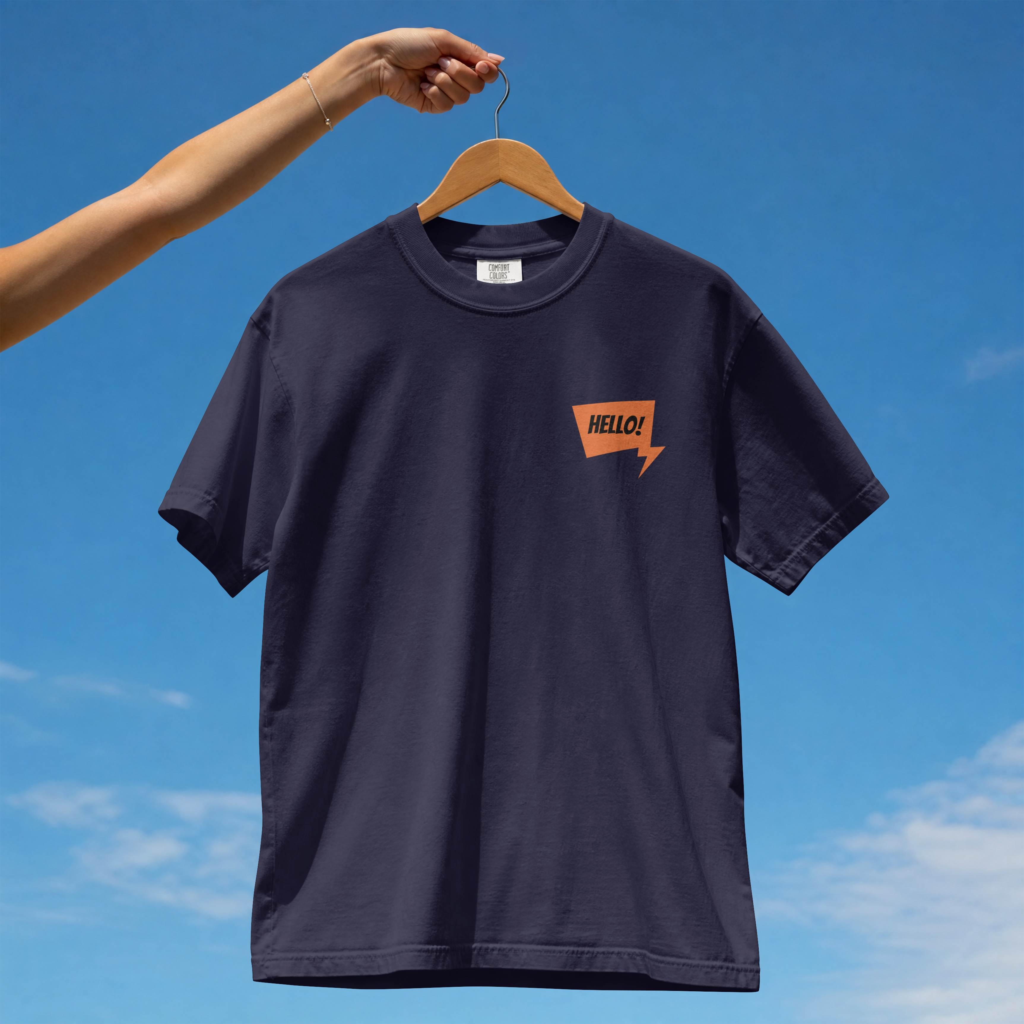 Front view of a premium cotton t-shirt with a small orange HELLO speech bubble badge printed on the left chest