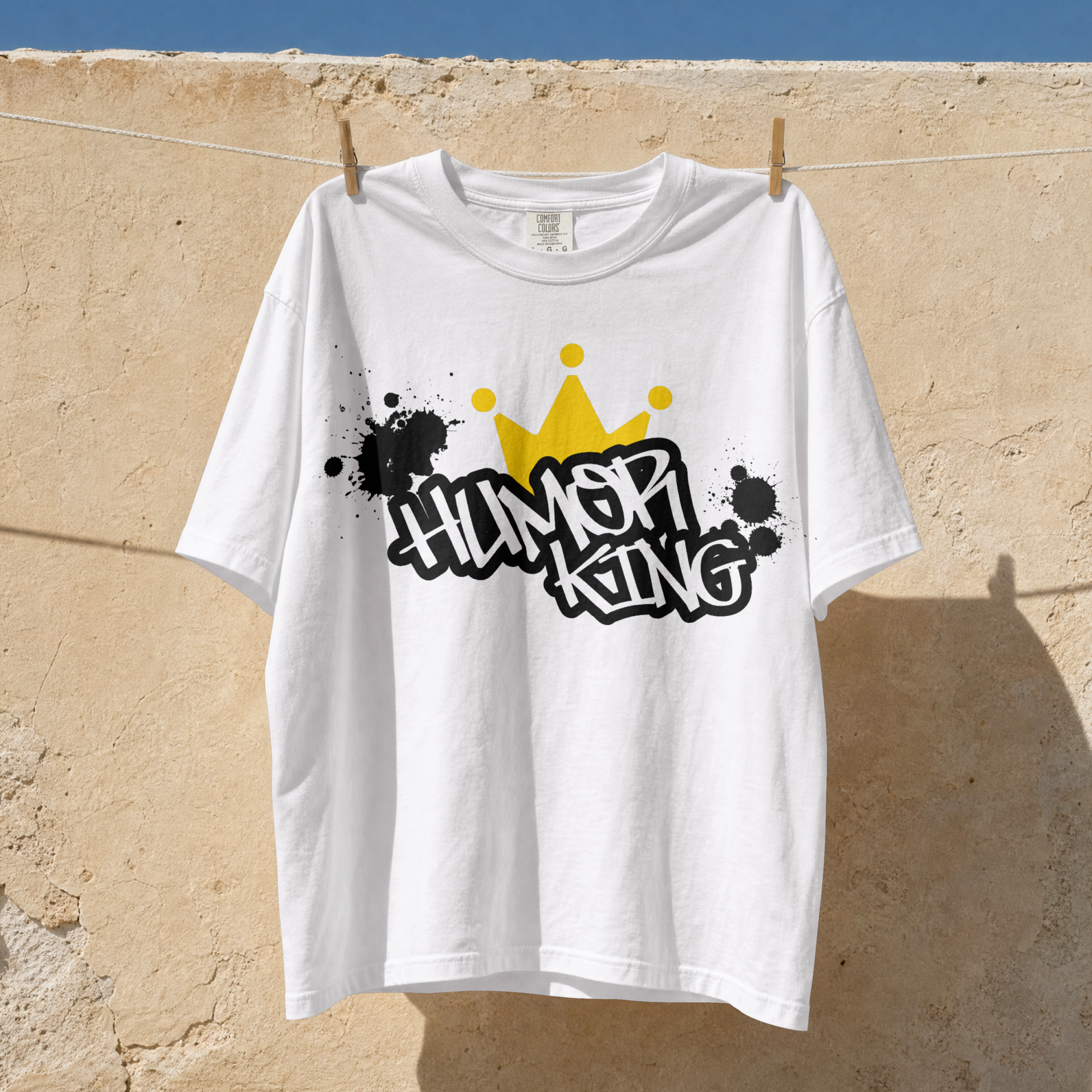 white relaxed fit streetwear t-shirt with a black paint splatter background, white Humor King typography, and a yellow crown